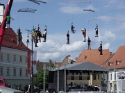 Einem Mobile gleich hängen Menschen an Kränen und spielen Musik