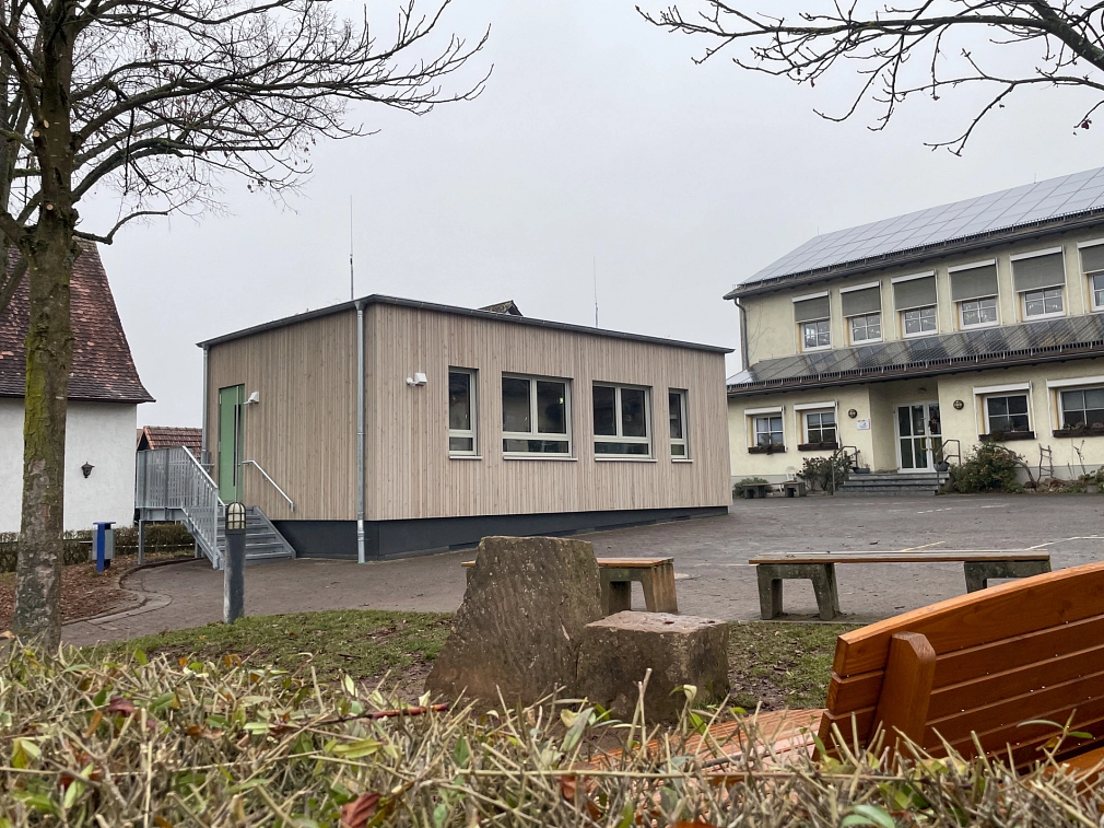 Eingeschossiger Holzmodulbau mit Treppe auf einem Schulhof. Im Hintergrund ein weiteres Gebäude, im Vordergrund Sitzbänke auf einer Grünfläche.&nbsp;&copy;&nbsp;Michael Kopatz, Stadt Marburg