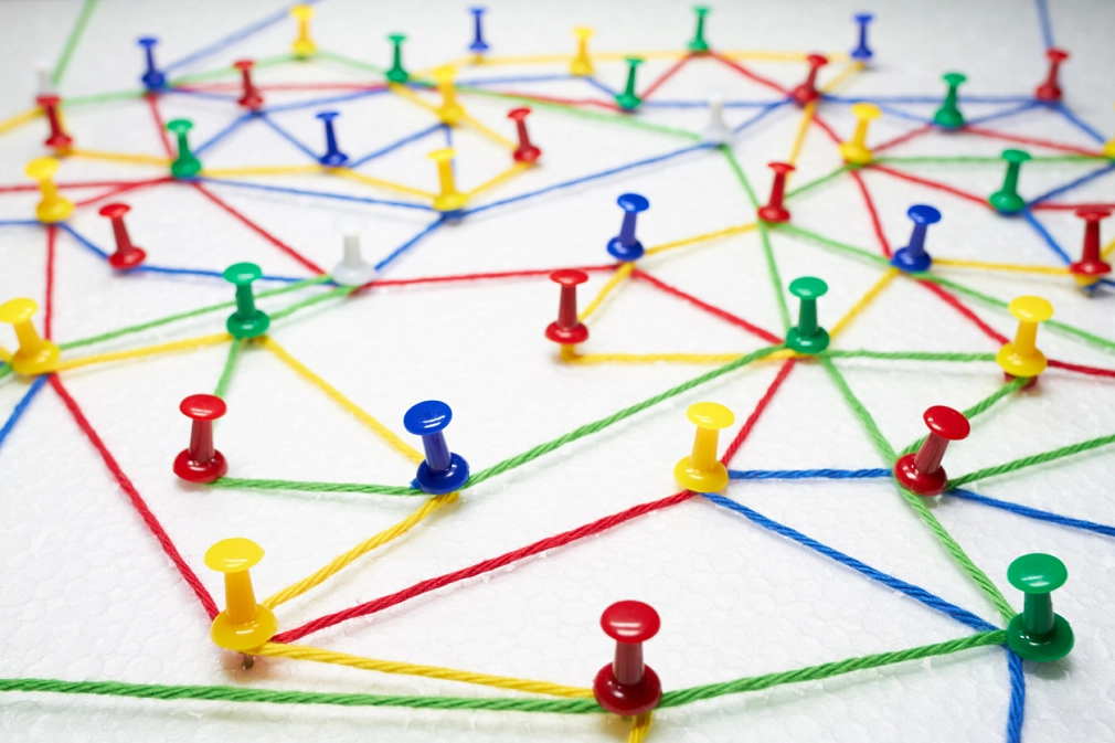 Netzwerke der Gesunden Stadt Rote, gelbe, grüne und blaue Wollfäden bilden ein Netzgeflecht zwischen roten, gelben, grünen und blauen Reißzwecken. © iStock_foto-ruhrgebiet