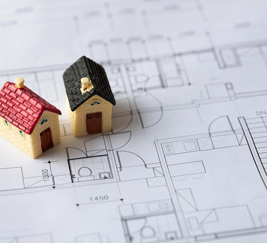 OptiWohnen Nahaufnahme: Zwei Miniaturhäuser stehen auf einer Architekturzeichnung.