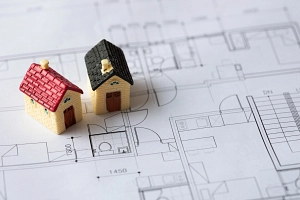 OptiWohnen Nahaufnahme: Zwei Miniaturhäuser stehen auf einer Architekturzeichnung.