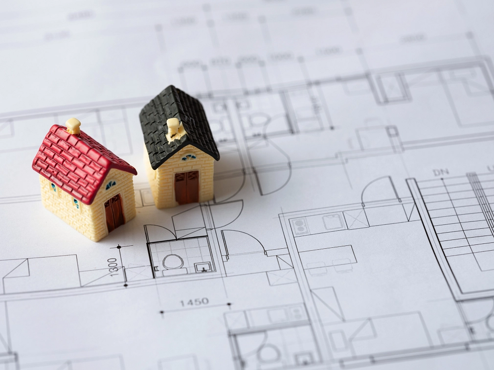 Nahaufnahme: Zwei Miniaturhäuser stehen auf einer Architekturzeichnung.