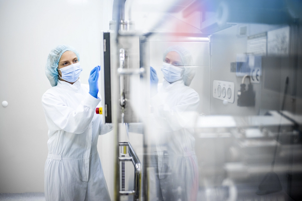 Pharmazeutische Industrie: Eine Frau in einem weißen Schutzanzug steht an dem Bildschirm einer großen Maschine.&nbsp;&copy;&nbsp;iStock / Extreme Media