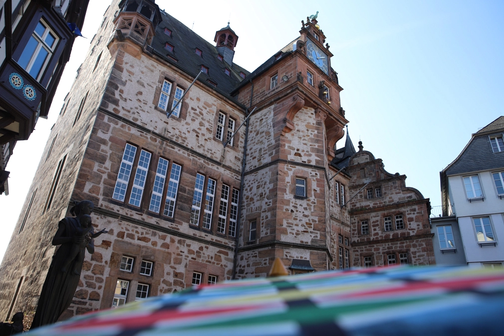 Schrägansicht des Marburger Rathauses, im Vordergrund Teile eines bunten Sonnenschirms.&nbsp;&copy;&nbsp;Dennis Siepmann, Stadt Marburg