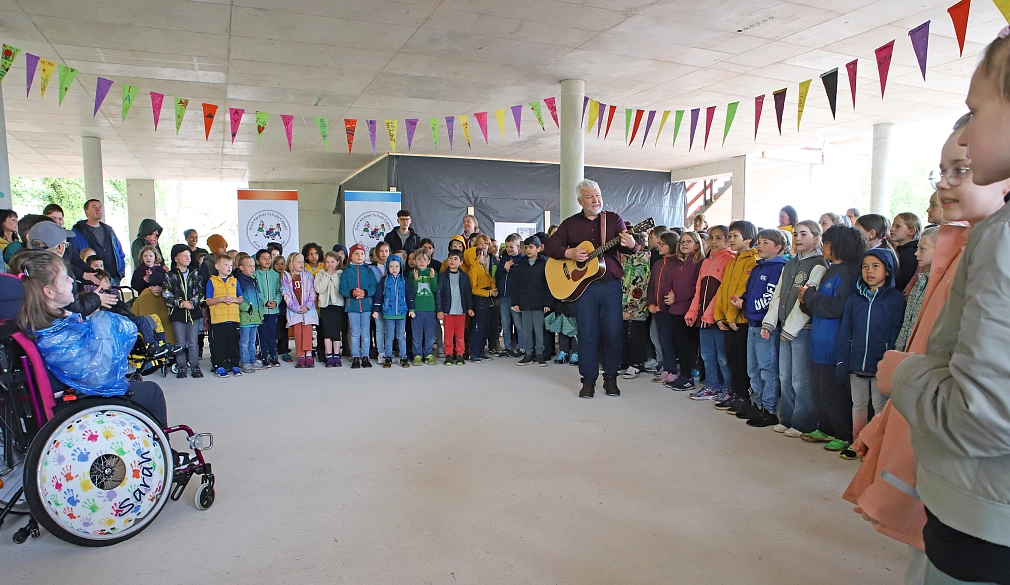 Viele Menschen stehen in einem Raum im Rohbauzustand. In der Mitte der Menschen steht ein Mann und spielt Gitarre. Der Raum ist mit vielen Wimpel-Girlanden geschmückt.