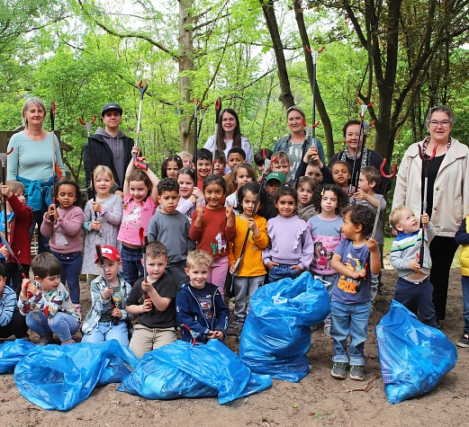 Eine Gruppe von Kindern stehen aufgestellt mit Müllzangen in der Hand in einem Wäldchen. Vor Ihnen liegen gefüllte blaue Säcke. Einige Erwachsene stehen in der hinteren Reihe.