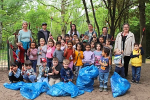 Sauberhafter Kindertag 2026 Eine Gruppe von Kindern stehen aufgestellt mit Müllzangen in der Hand in einem Wäldchen. Vor Ihnen liegen gefüllte blaue Säcke. Einige Erwachsene stehen in der hinteren Reihe.