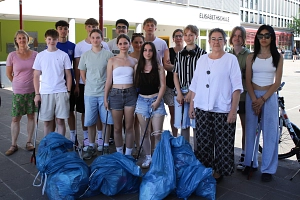Eine Gruppe von Menschen steht vor einem Gebäude. Einige von Ihnen halten Greifzangen in der Hand. Vor ihnen liegen gefüllte blaue Säcke.