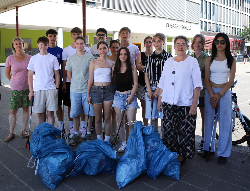 Eine Gruppe von Menschen steht vor einem Gebäude. Einige von Ihnen halten Greifzangen in der Hand. Vor ihnen liegen gefüllte blaue Säcke.