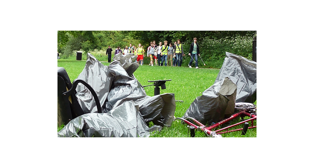 Sauberhafter Schulweg_Abfallsäcke Das Foto zeigt Abfallsäcke und einen Fahrradrahmen ohne Reifen im Vordergrund. Dahinter gehen Kinder in Warnwesten mit Papierzangen und sammeln Abfälle ein. © DBM, Sonja Stender