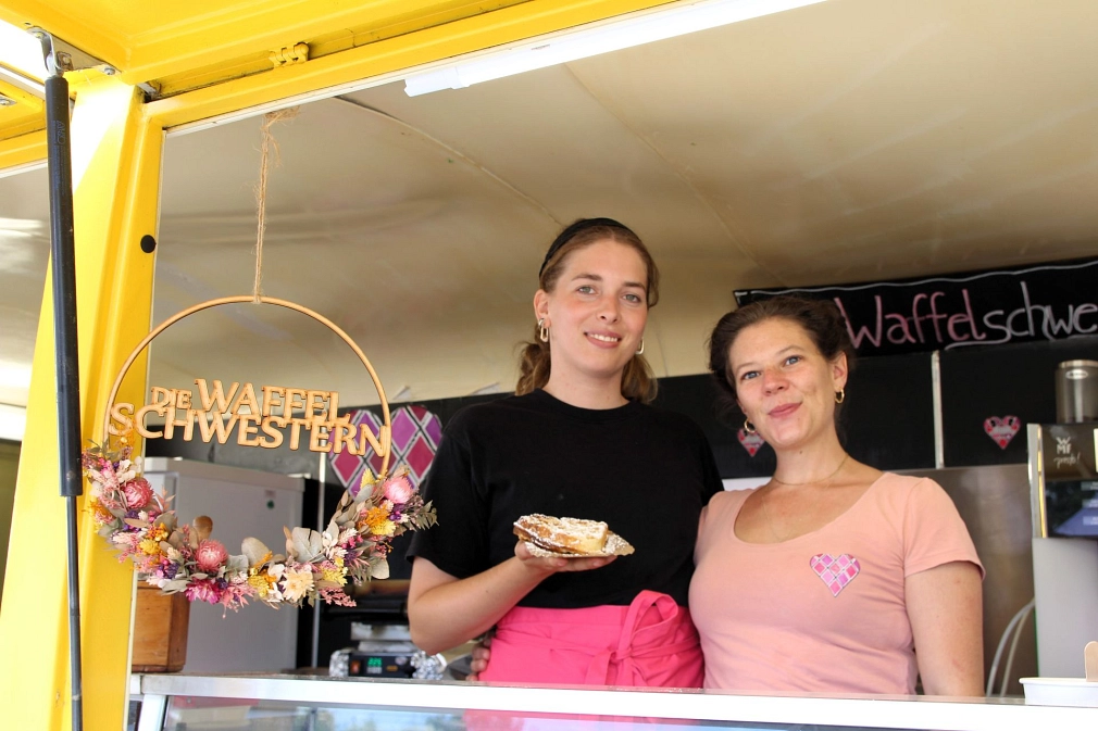Zwei Frauen stehen in einem Foodtruck. Eine Frau hält eine Waffel in der Hand.