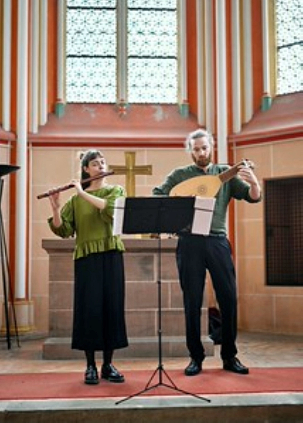 Zwei Personen spielen jeweils ein Streichinstrument in einem gemauerten Gebäude. Vor ihnen steht ein Notenständer.