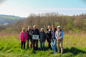 Sieben Personen stehen in der Natur. Hinter ihnen sieht man Wiesen und Sträucher.