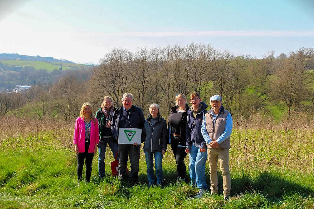 Sieben Personen stehen in der Natur. Hinter ihnen sieht man Wiesen und Sträucher.