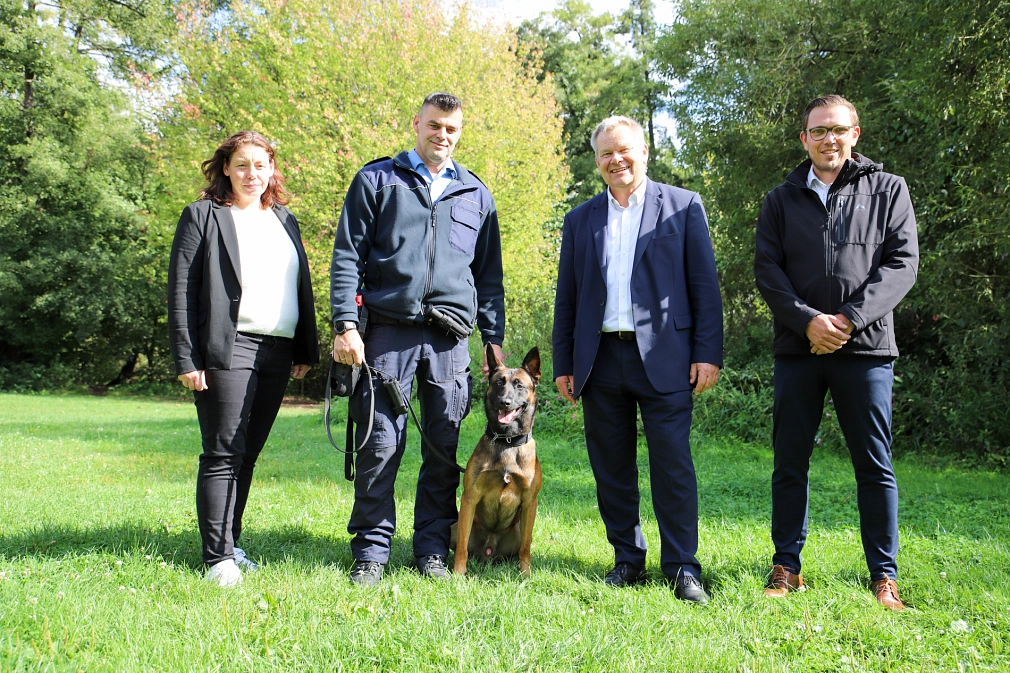 Vier Menschen und ein Hund stehen auf einer Wiese und schauen in die Kamera.