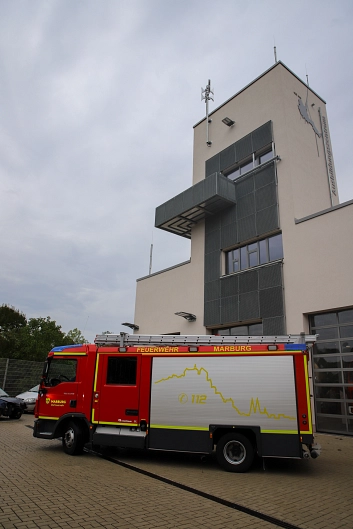 Eine Sirene auf einem Turm, davor steht ein Feuerwehrwagen.