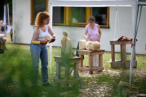 Sommerakademie: Kurs Lilian Hasler, Holz-Bildhauerei Kursteilnehmer*innen arbeiten im Freien an Holzskulpturen.