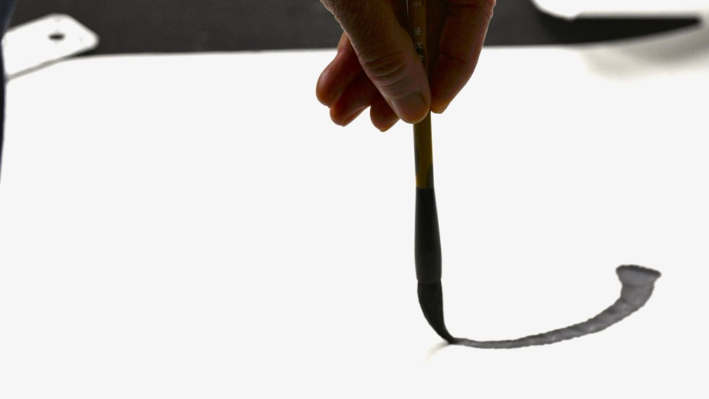 Hand führt einen Pinsel und mal einen schwarzen Tuschestrich auf ein großes weißes Blatt.&nbsp;&copy;&nbsp;Georg Kronenberg
