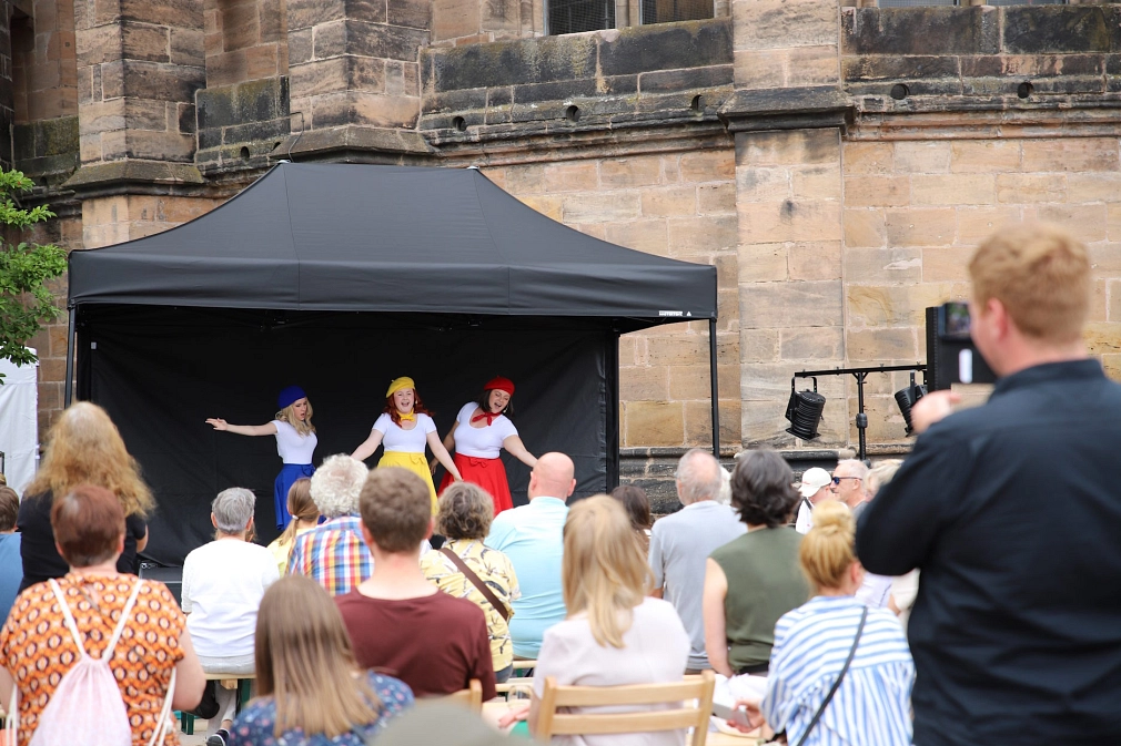 Sommertheater auf dem Firmaneiplatz: Drei Frauen singen und tanzen auf einer Bühne. Das Publikum sitzt davor.