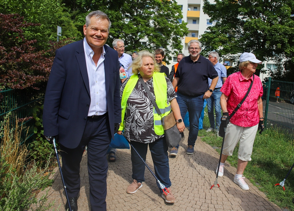 Einige Personen laufen auf einem Weg. In der Hand halten sie Müllzangen.
