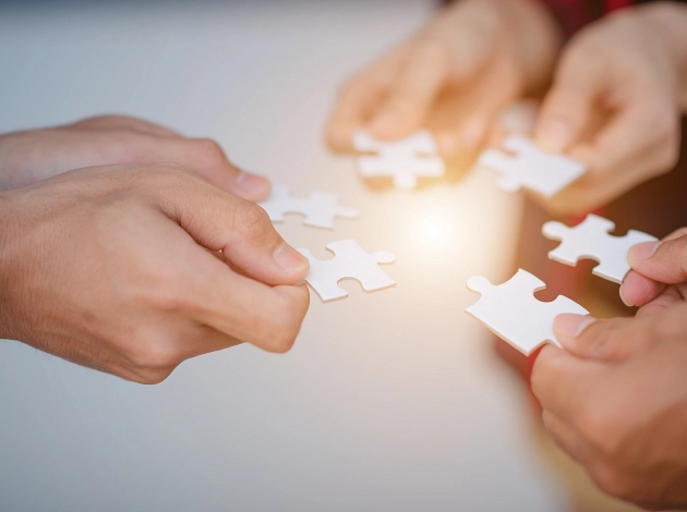 Nahaufnahme mehrerer Hände. Jede Hand hält ein Puzzleteil.