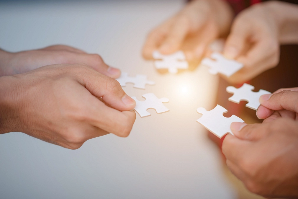 Sozialplanung der Stadt Marburg Nahaufnahme mehrerer Hände. Jede Hand hält ein Puzzleteil. © iStock/KBL Studio