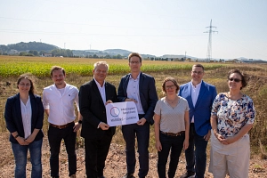 Das Bild zeigt sieben Personen vor einem Acker. Die beiden mittleren Personen halten ein Schild mit der Aufschrift 'Industriegebiet Spiegelshecke Marburg-Lahntal' in die Kamera.