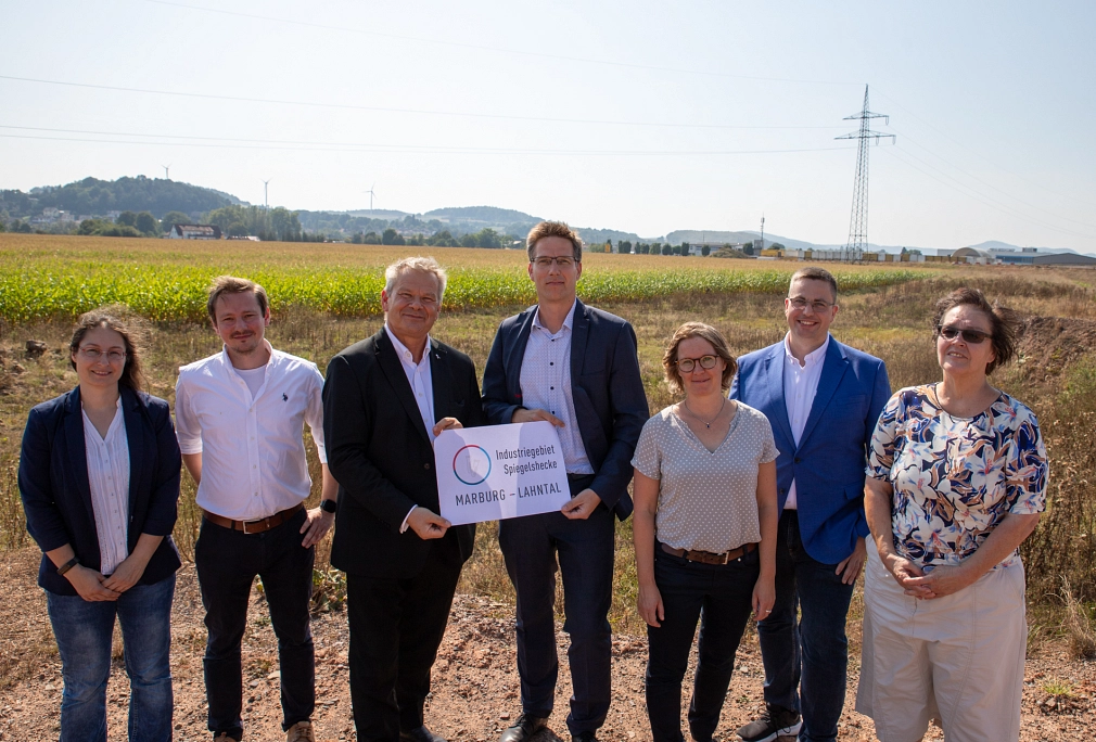 Das Bild zeigt sieben Personen vor einem Acker. Die beiden mittleren Personen halten ein Schild mit der Aufschrift 'Industriegebiet Spiegelshecke Marburg-Lahntal' in die Kamera.&nbsp;&copy;&nbsp;Patricia Grähling, Stadt Marburg