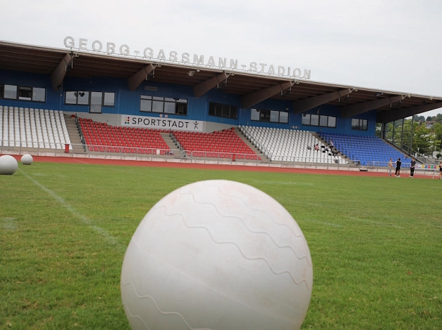 Blick auf die Tribüne des Georg-Gaßmann-Stadions, im Vordergrund liegt ein Ball auf dem Rasen.