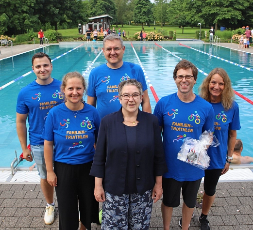 Sportlerehrung Volker Sonthoff Auf dem Bild sieht man 6 Personen, die vor einem Schwimmbecken stehen. Eine der vorderen Personen wurde geehrt und trägt ein kleines Geschenk in ihren Händen.