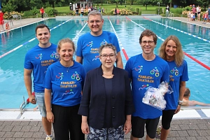 Sportlerehrung Volker Sonthoff Auf dem Bild sieht man 6 Personen, die vor einem Schwimmbecken stehen. Eine der vorderen Personen wurde geehrt und trägt ein kleines Geschenk in ihren Händen.