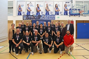 Sportplakette Blue Dolphins Eine Basketballmannschaft ist versammelt in einer Turnhalle. Dort wird ein Bild von Ihnen gemacht, wo sie die Sportplakette in Silber um den Hals tragen.