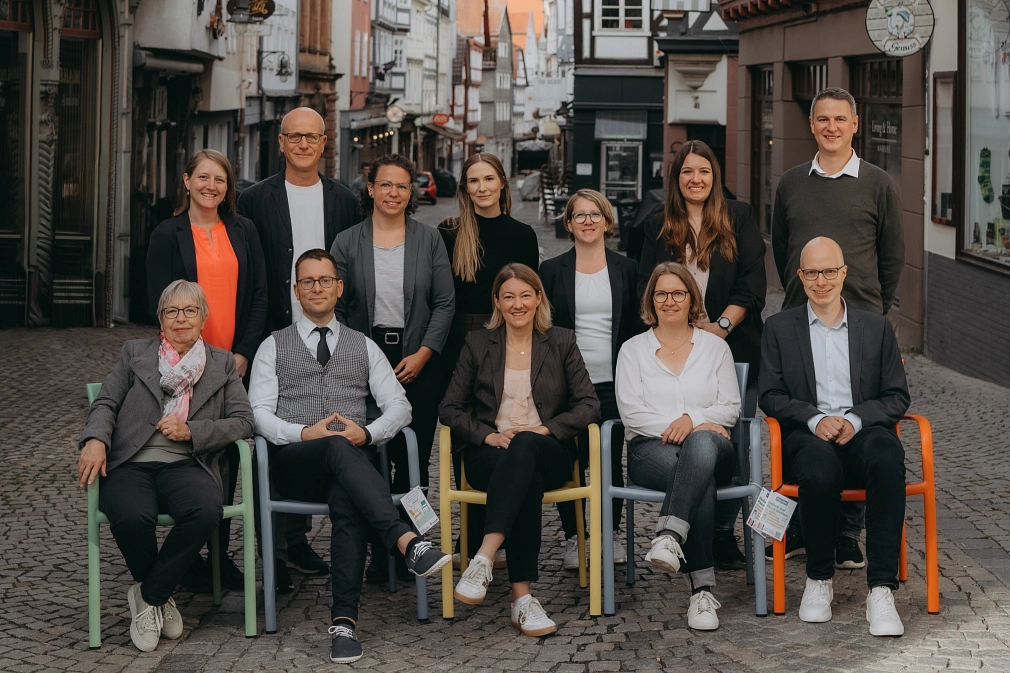 Stabsstelle 15_2025_Gruppenbild Gruppenfoto vom Team der Wirtschaftsförderung in der Barfüßer Straße. Einige Personen sitzen auf Stühlen, andere sitzen dahinter. © Universitätsstadt Marburg