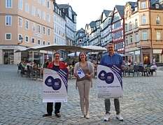 Auf dem Marktplatz stehen Stadträtin Kirsten Dinnebier, Björn Backes und Jana Kahler und halten Plakate in der Hand. © Stefanie Ingwersen, Stadt Marburg