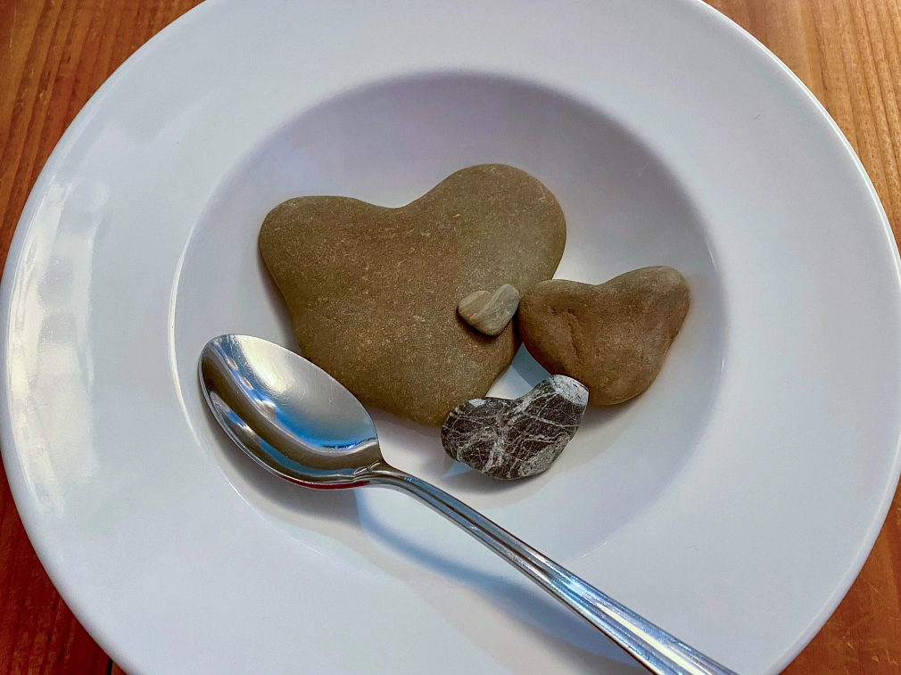 "Steinsuppe" in der Stadtbücherei In einem Suppenteller befinden sich vier Steine, die wie Herzen geformt sind, ein Löffel liegt daneben. © Simone Batz, Stadt Marburg