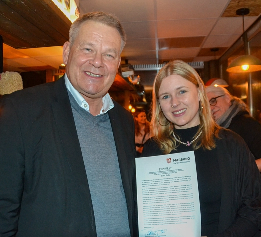 Stipendium Gina Bolle 1 Das Bild zeigt den Oberbürgermeister mit einer weiteren Person, in die Kamera lächeln. Die Person hält ein Zertifikat in der Hand.