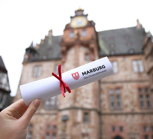 Symbolbild_Jugendföderstipendium Ein gerolltes Papier mit einer roten Schleife vor dem Rathaus.