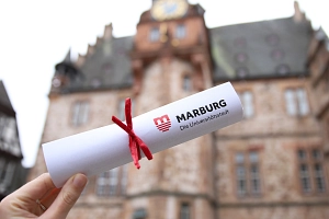 Symbolbild_Jugendföderstipendium Ein gerolltes Papier mit einer roten Schleife vor dem Rathaus.