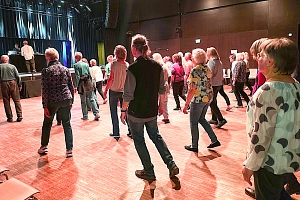Tanz der Generationen 2025 Viele Menschen stehen in einem Gebäude in Reihen und tanzen.