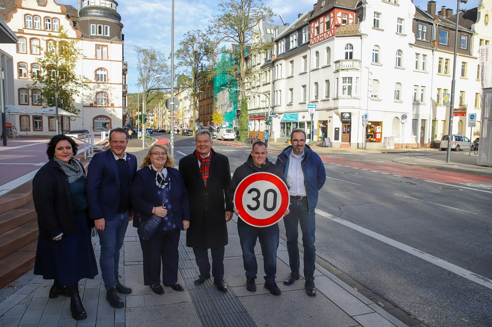 Sechs Personen stehen an einer Straße. Einer von Ihnen hält ein Straßenschild mit der Zahl 30 in den Händen.