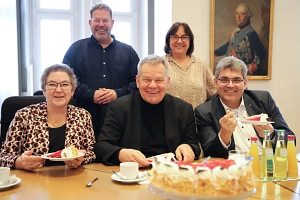Thedodor-Schubert-Stiftung 2025 Fünf Personen sitzen an einem Tisch. Auf dem Tisch stehen Getränke und Kuchen. Alle lächeln in die Kamera.