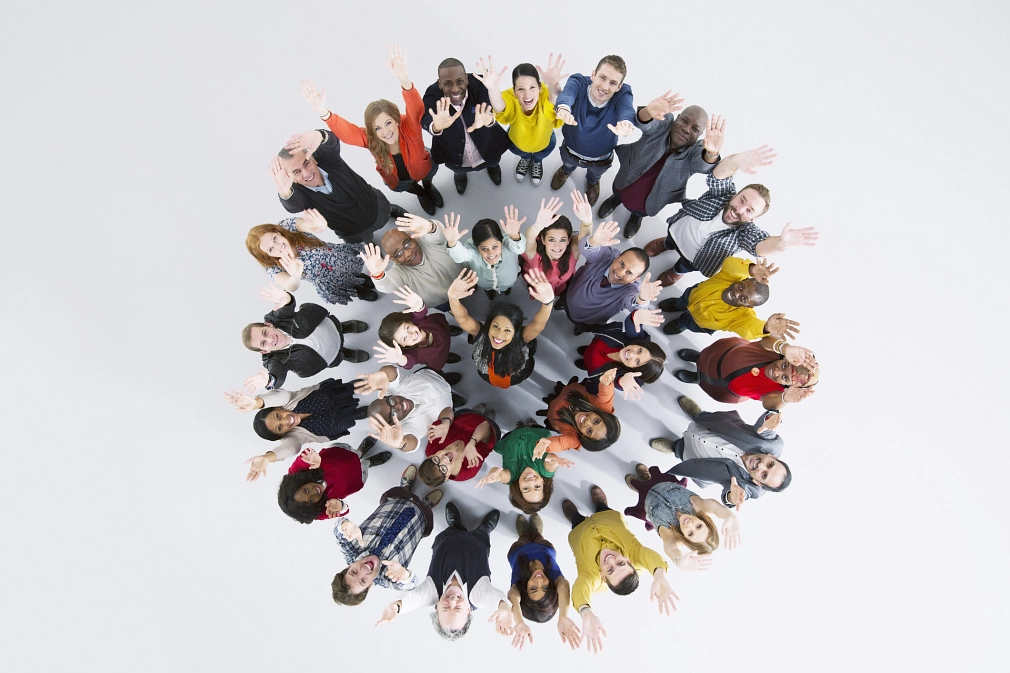 Luftaufnahme einer Gruppe von fröhlichen Menschen im Kreis. Sie heben die Hände und schauen in die Kamera.&nbsp;&copy;&nbsp;iStock / Caiaimage/Martin Barraud