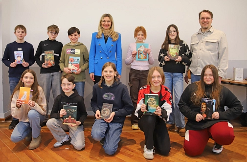 Zehn Kinder und zwei Erwachsene lächeln in die Kamera. Die Kinder halten jeweils ein Buch in der Hand.