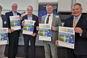 Sechs Männer stehen im Halbkreis vor einer Leinwand. Alle halten ein kleines Plakat in den Händen.