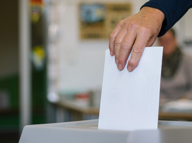 Eine Person wirft einen Wahlumschlag in eine Wahlurne. Zu sehen ist nur die Hand.